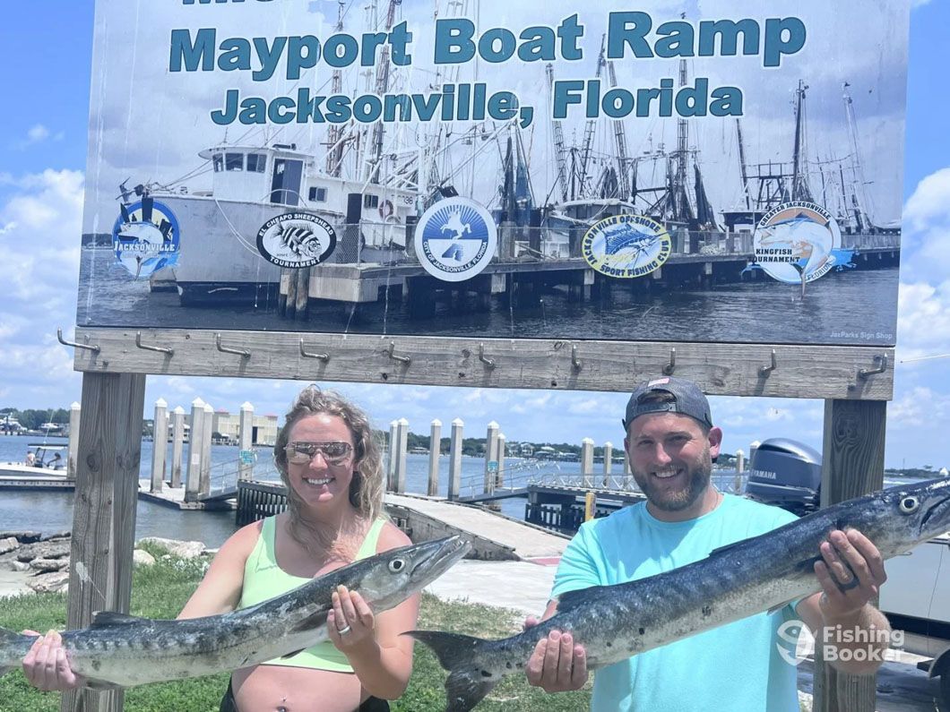 A man and a woman are holding two large fish in front of a sign.