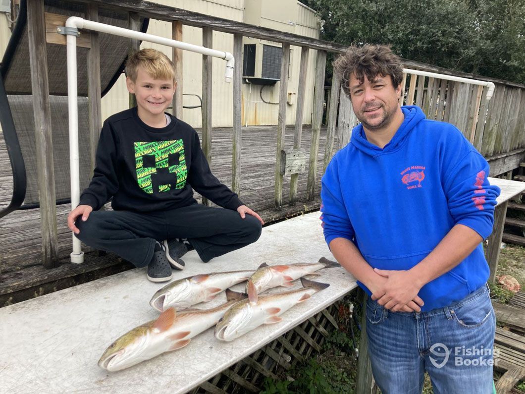 A man and a boy are standing next to a table with fish on it.