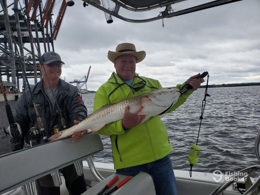 Two men are standing on a boat holding a large fish.