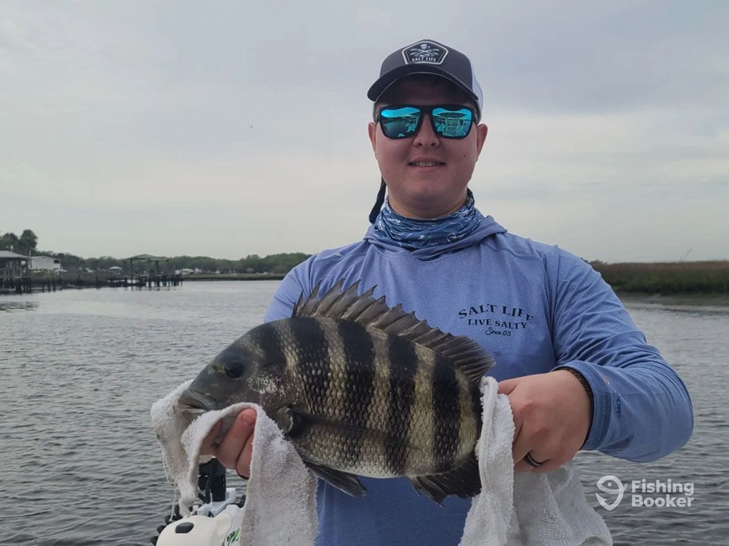 A man is holding a large fish in his hands in front of a body of water.