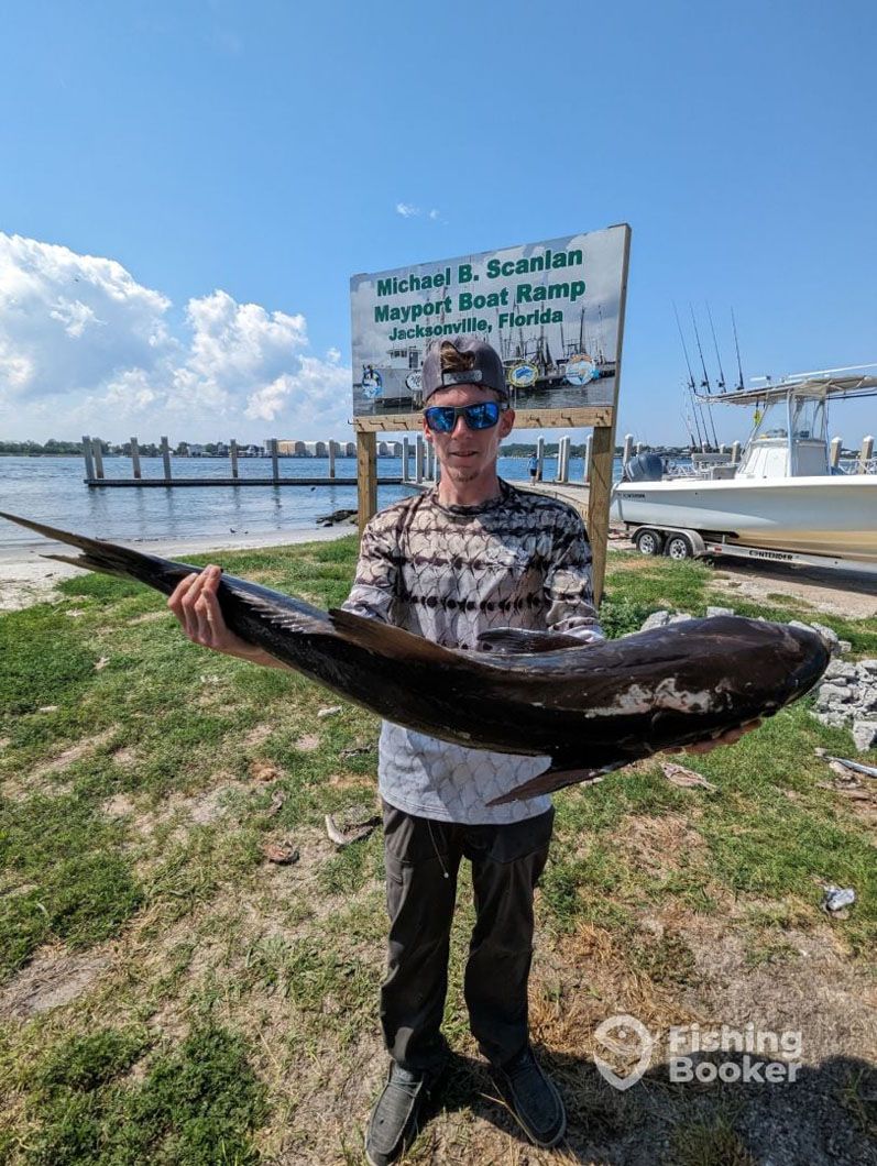 A man is holding a large fish in front of a sign.