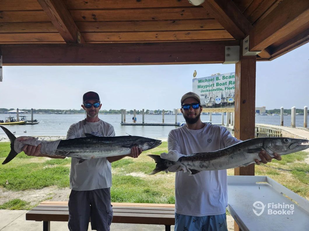 Two men are holding two large fish under a pavilion.