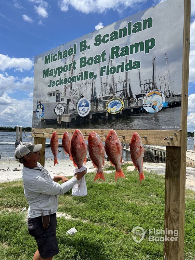 A man is holding a bag of fish in front of a sign.