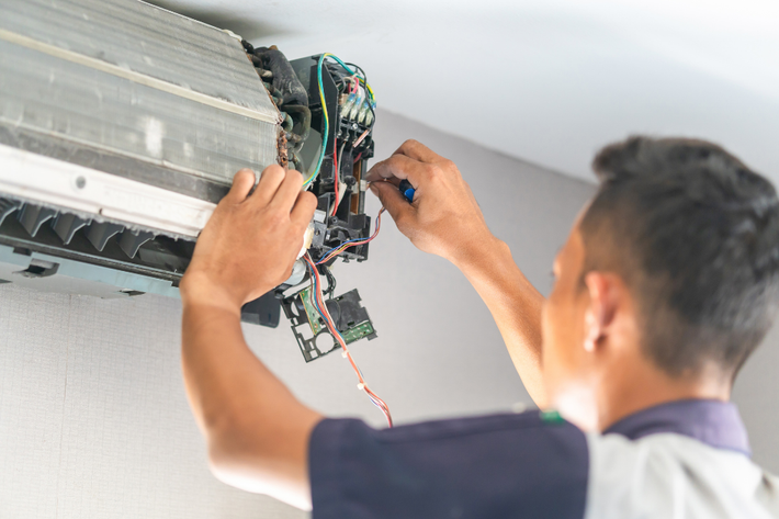 A man is fixing an air conditioner with a screwdriver.