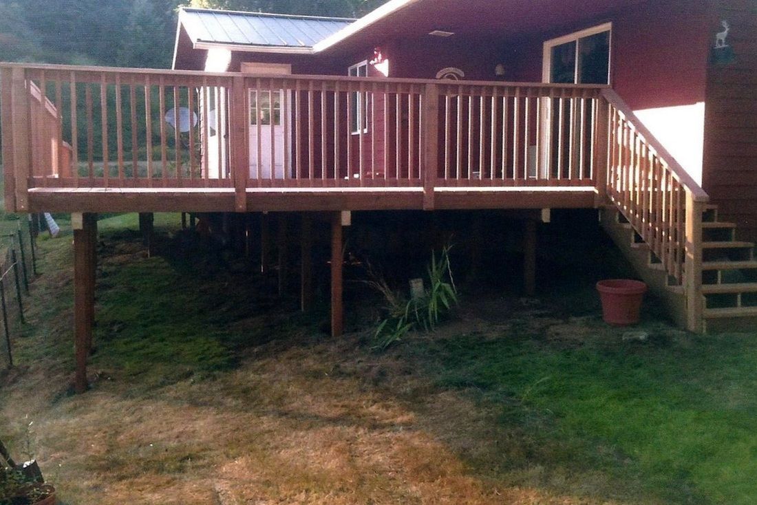 Wooden deck elevated on posts attached to a red house, with stairs leading to the ground.