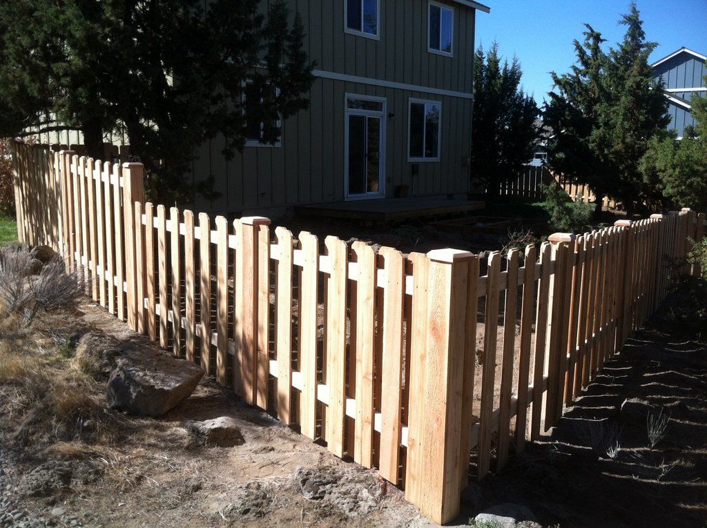 Wooden picket fence surrounding a two-story beige house under a clear sky.