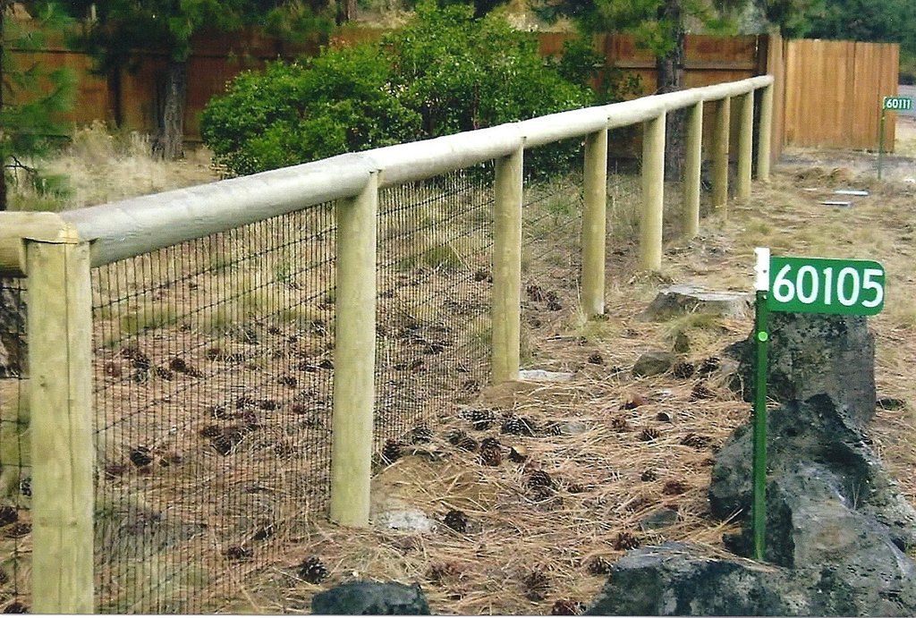 Wooden fence with vertical posts and horizontal top rail; green address sign.