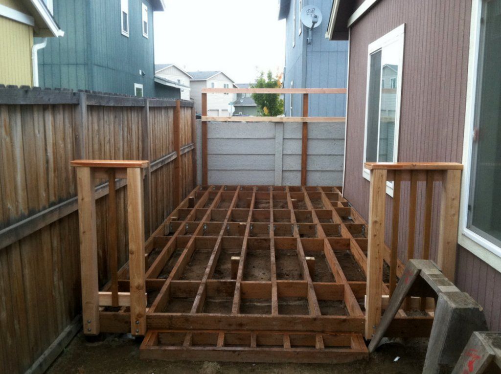 Wooden deck frame under construction in a yard, with partial fencing and house siding.