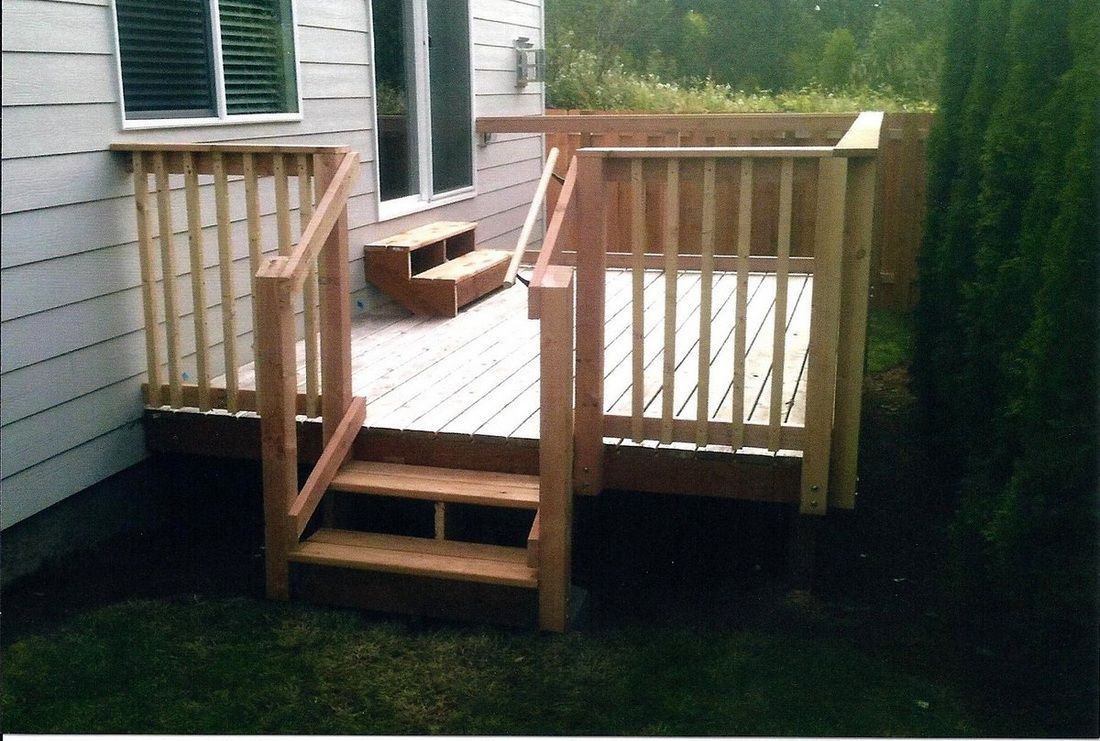 Wooden deck with railing and steps next to a house with a window and a door.
