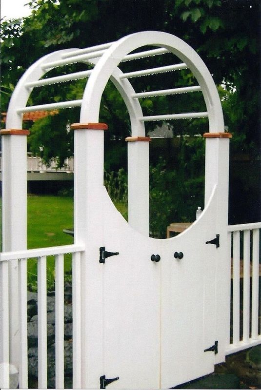 White wooden garden gate with an arched trellis and red-capped columns.