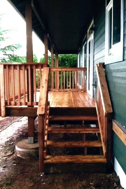 Wooden porch with stairs and railing leading to a house with green siding and white trim.