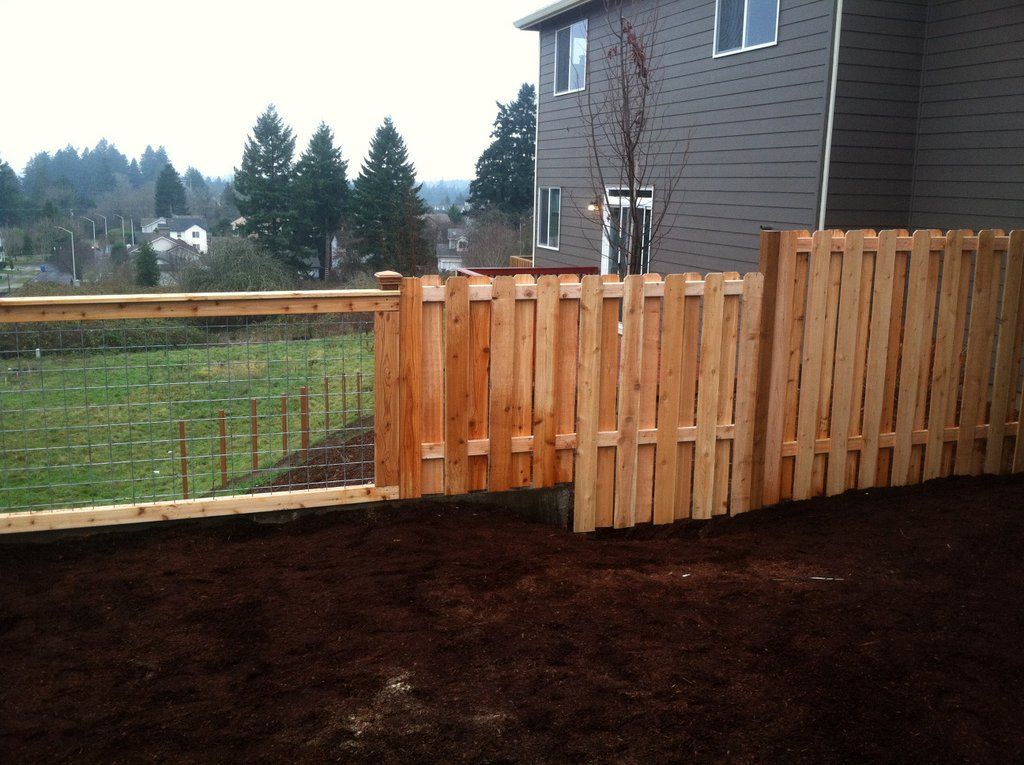 Wooden fence partially enclosing a backyard with a house in the background. Mulch covers the ground.