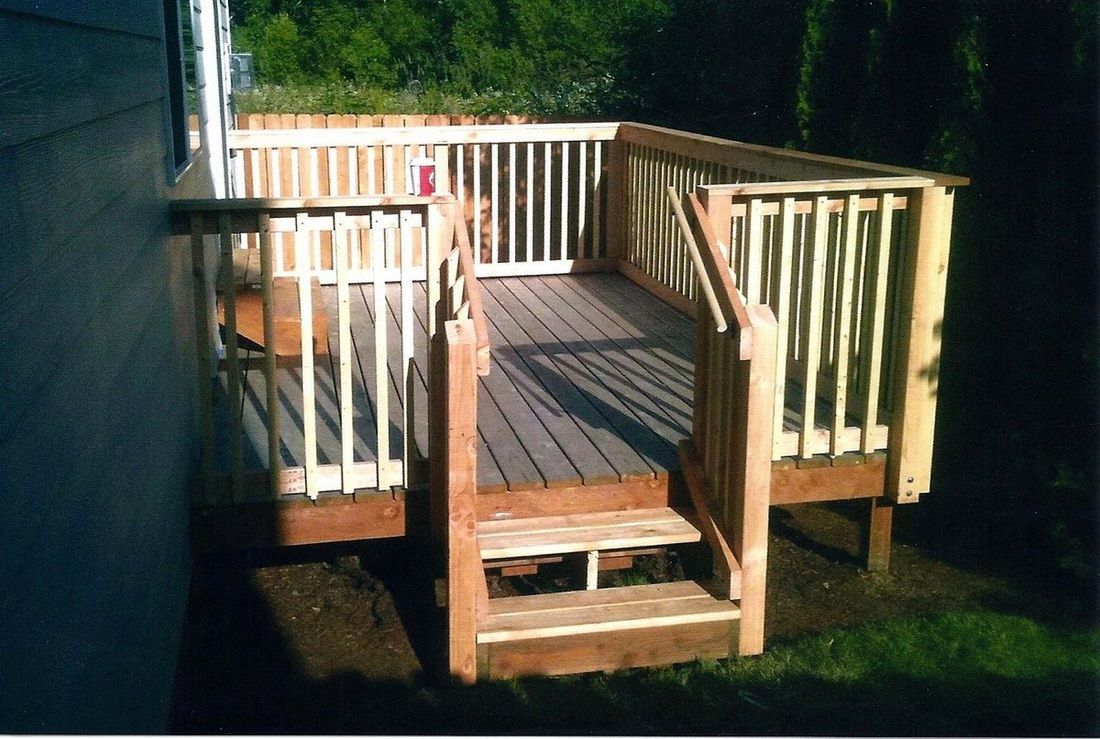 Wooden deck with stairs, built against a house. Railings and sunlight.
