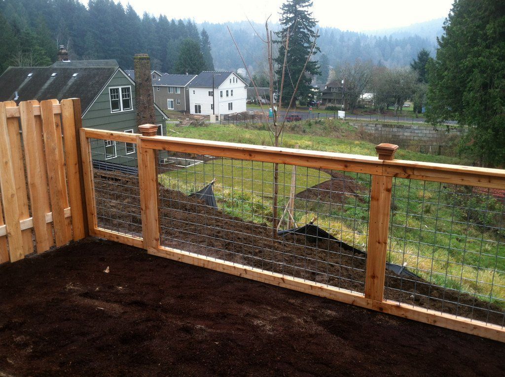 Wooden fence with wire mesh panels, overlooking a valley with houses and trees.
