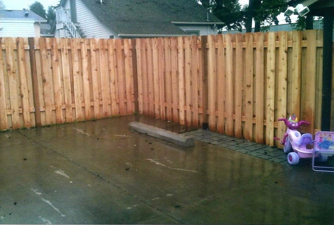 Wooden fence encloses a wet concrete patio. A child's toy is visible on the right.