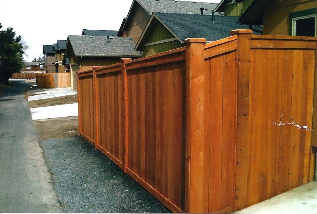 Wooden fence in front of houses; brown wood, gray asphalt, cloudy sky.