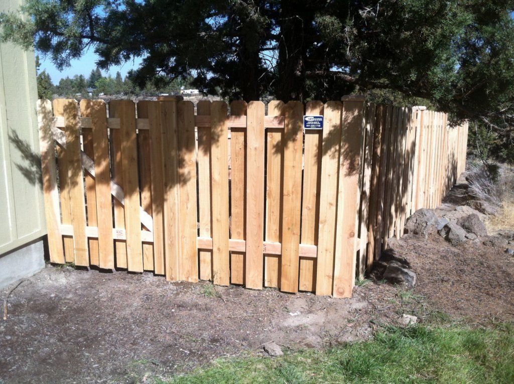 Wooden fence against a building and a tree, brown, outdoor setting.