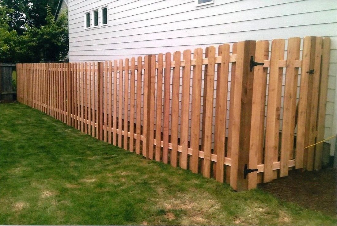 Wooden fence with a gate in a grassy backyard, adjacent to a white house with windows.