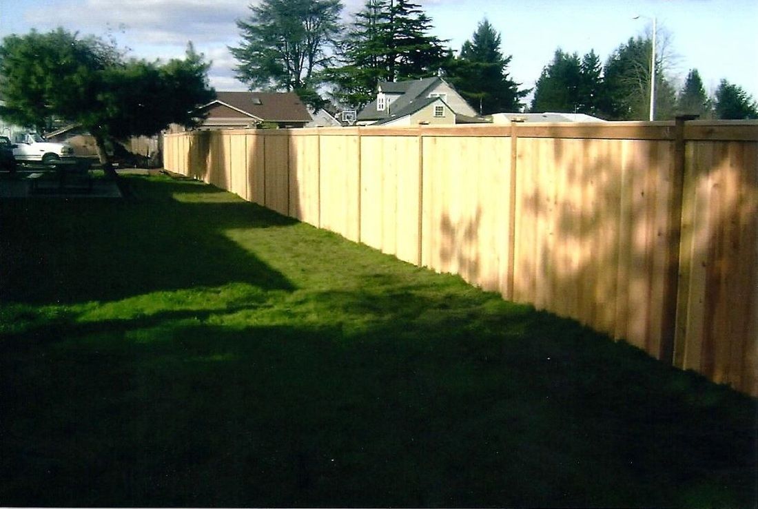 Wooden fence along green lawn, with houses and trees in the background.