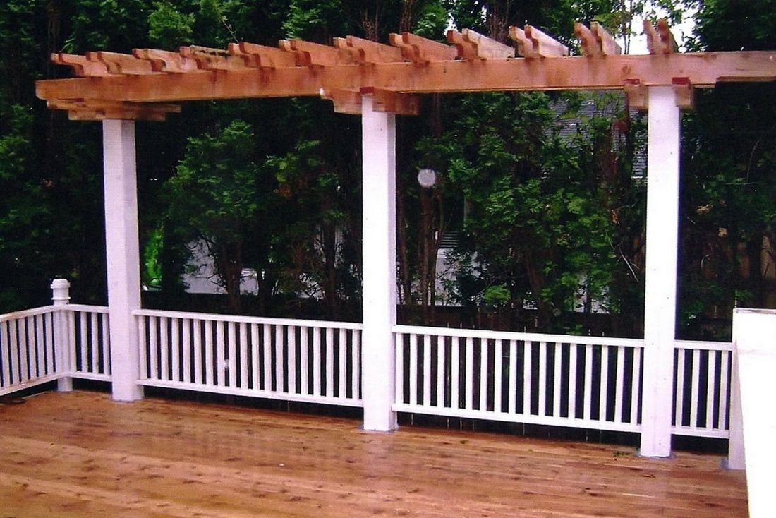 Wooden pergola with white columns and railing on a wooden deck.