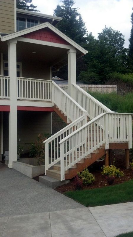 White staircase leads to a covered porch with red accents. Landscaped yard and concrete path below.