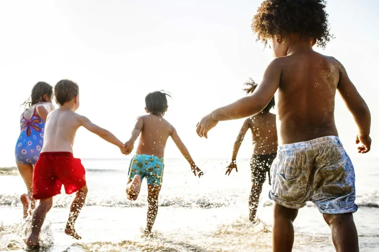 A group of children are running on the beach holding hands.