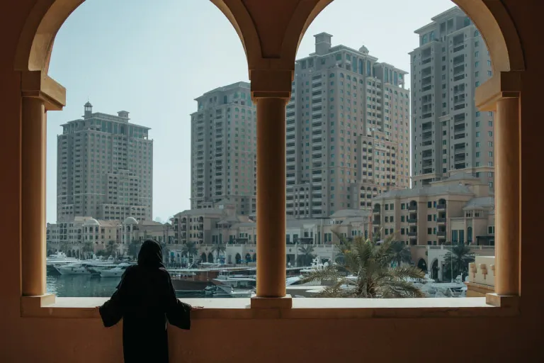 A woman is standing in front of a window looking out at a city.