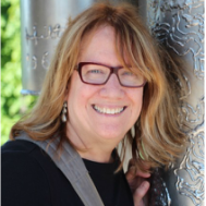 A woman wearing glasses is smiling and leaning against a pole.