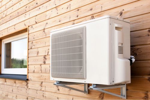 An Air Conditioner is Mounted on the Side of a Wooden House Next to a Window — JHE Air Conditioning Services In Saratoga, NSW
