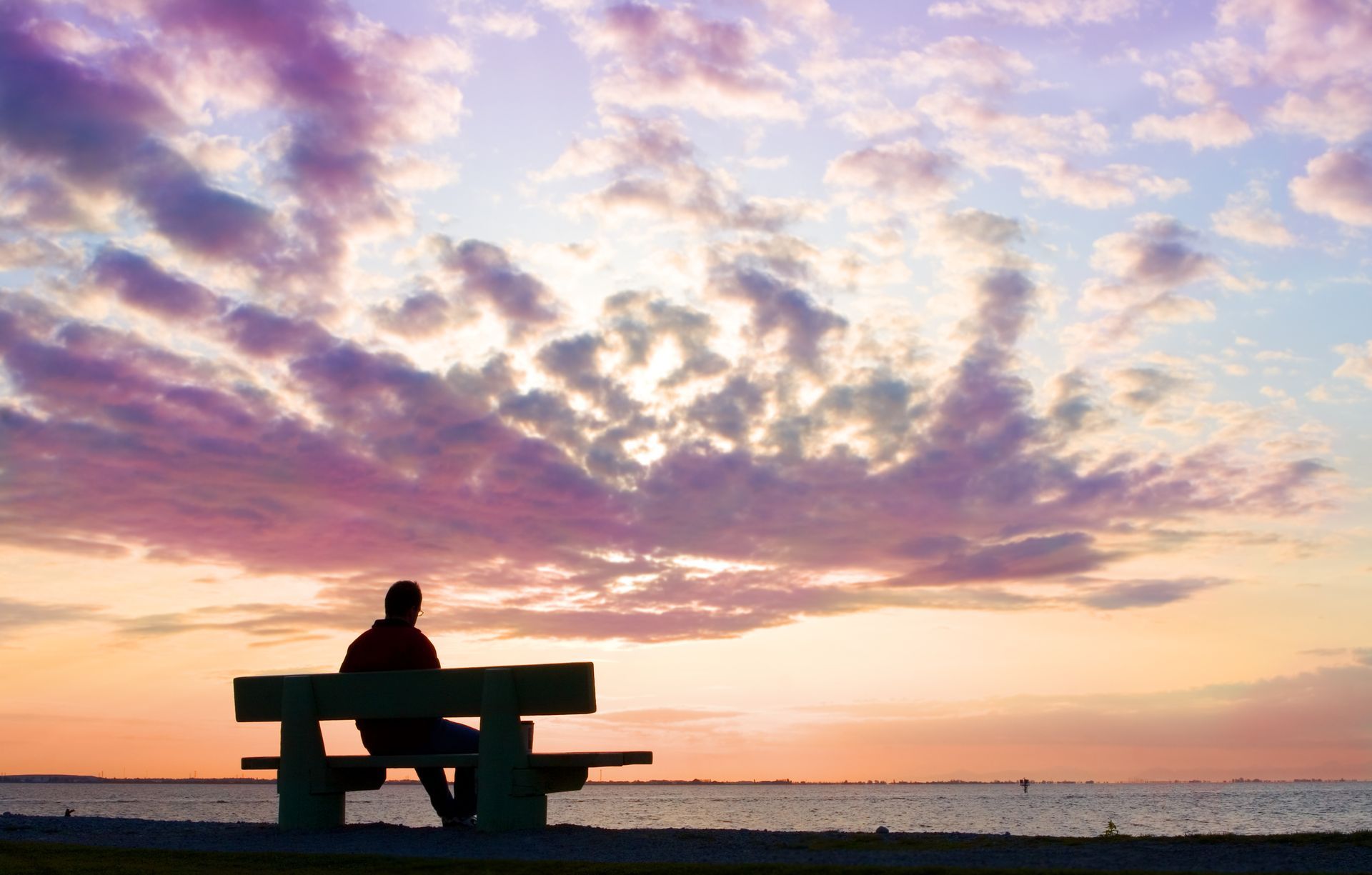 A person is sitting on a bench overlooking the ocean at sunset.
