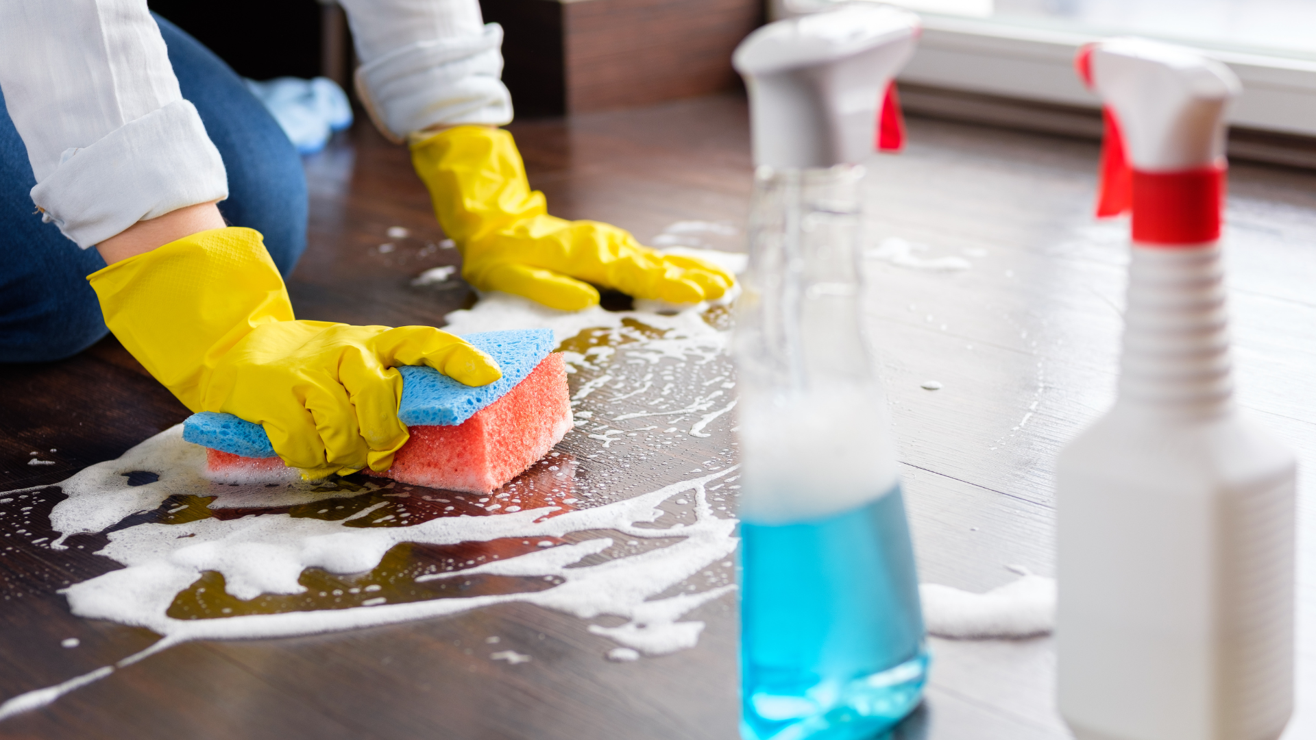 A person is cleaning a counter with a sponge and spray bottles.