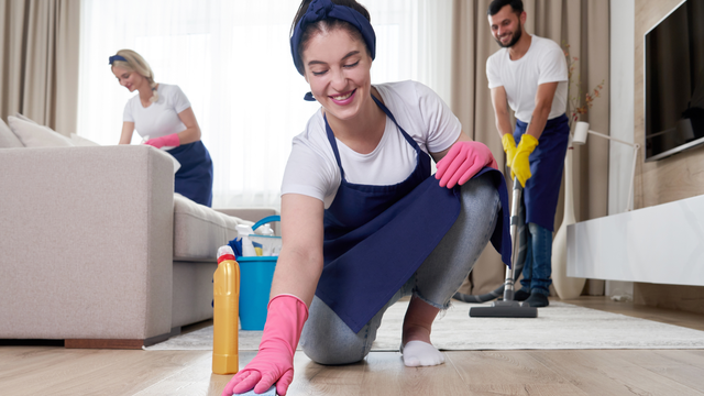 A woman in pink gloves is cleaning the floor in a living room.