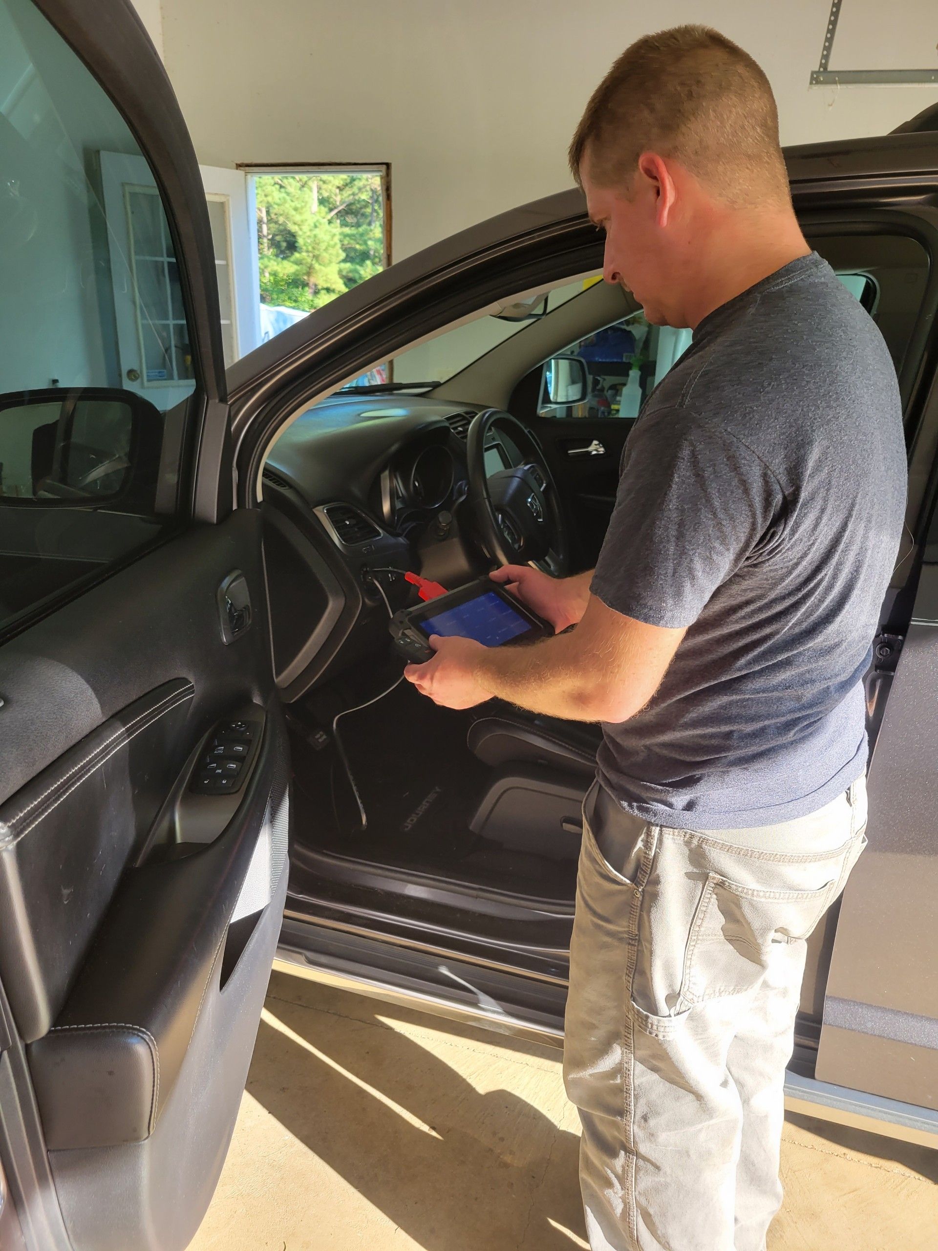A man is standing next to a car in a garage using a tablet.