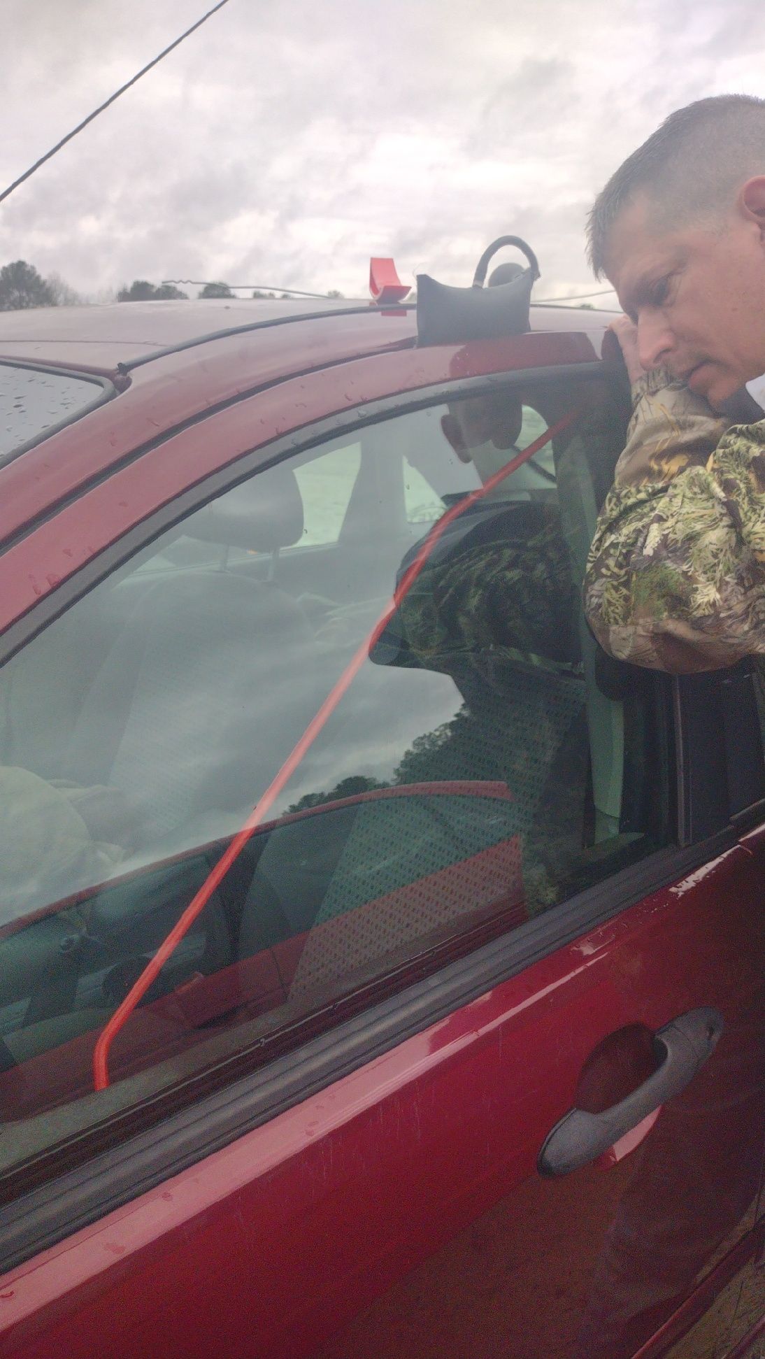 A man is sitting in a red car looking out the window.
