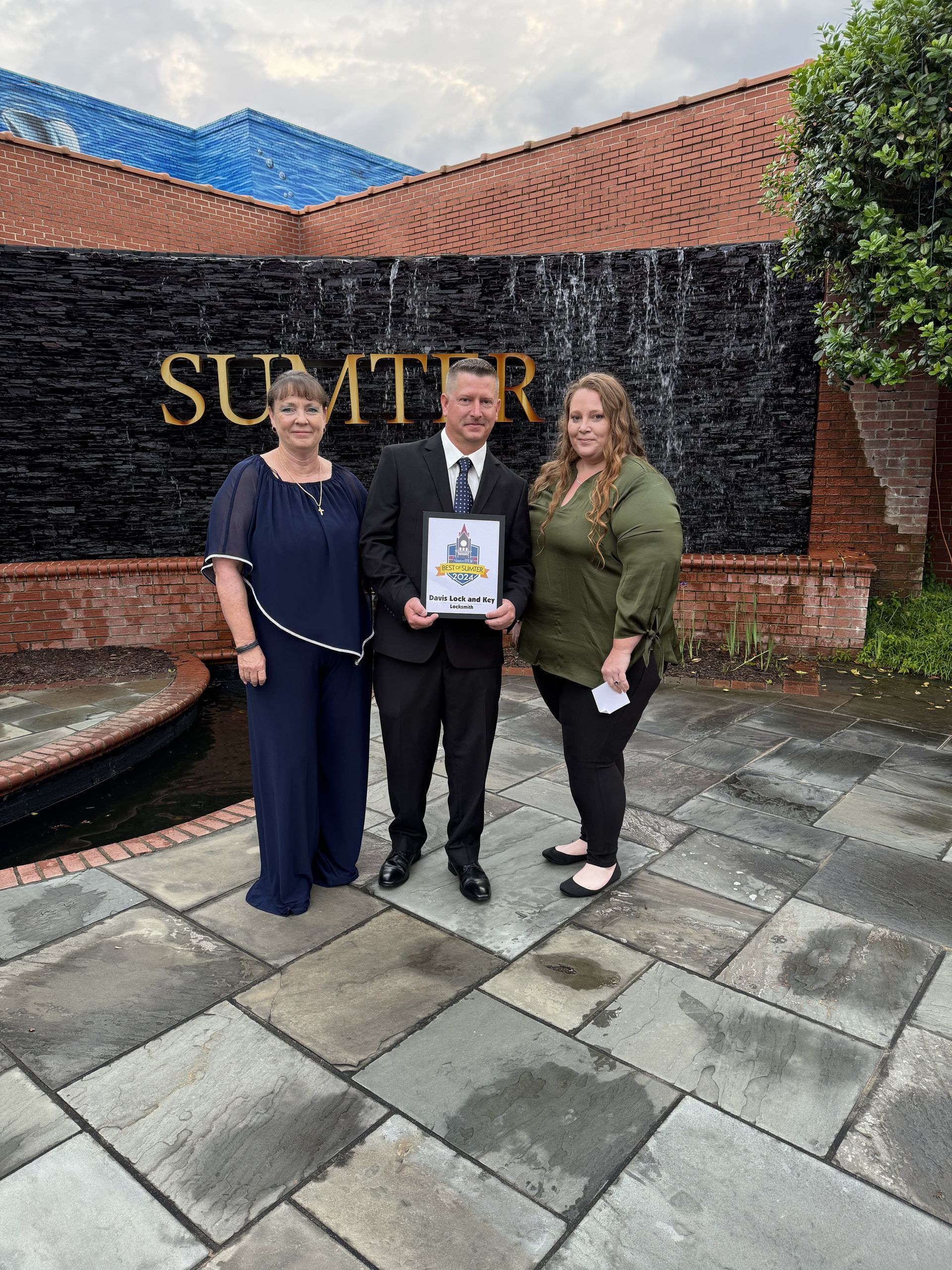 A man and two women are standing in front of a building holding a certificate.