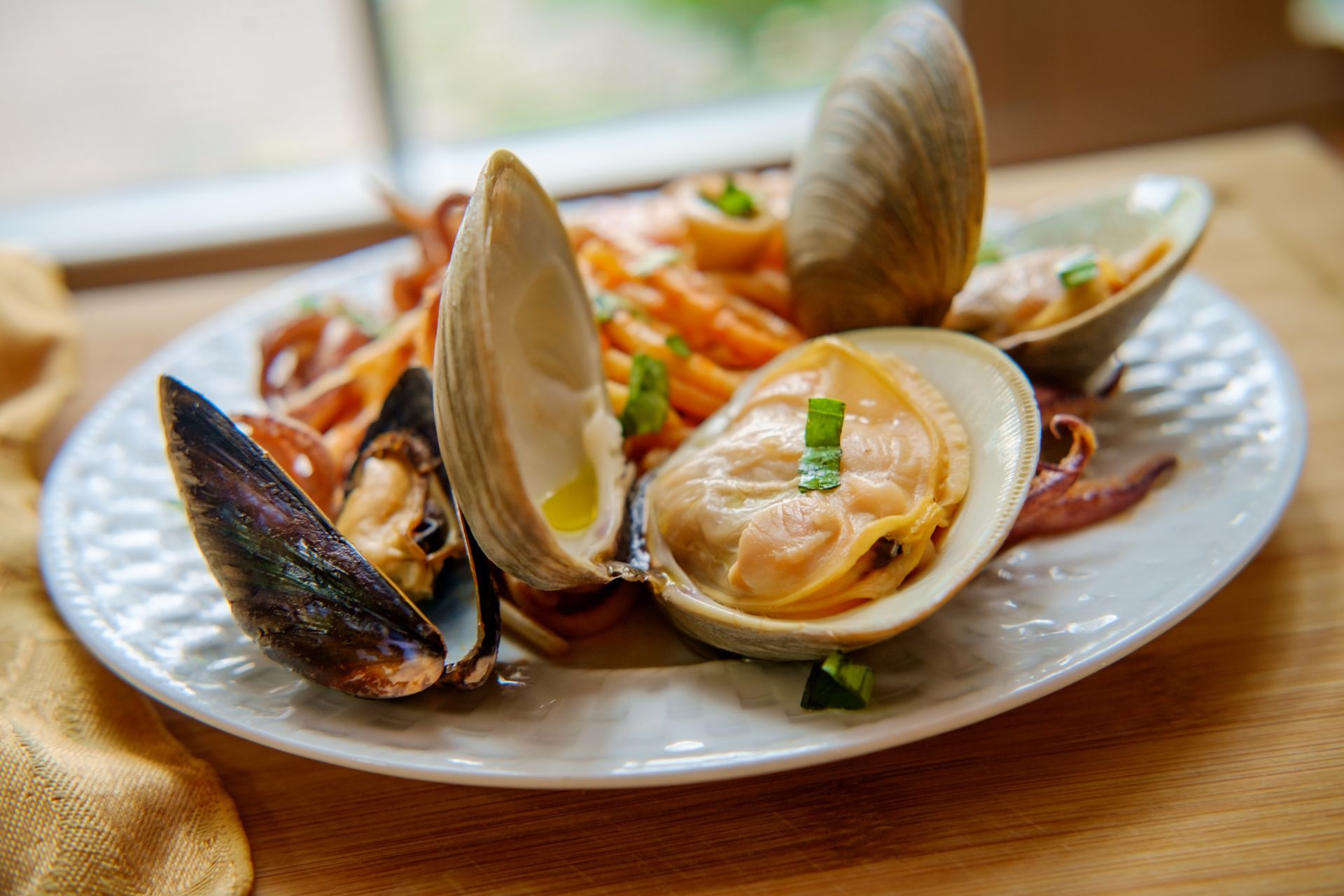 Un piatto bianco con vongole e spaghetti su un tavolo di legno.