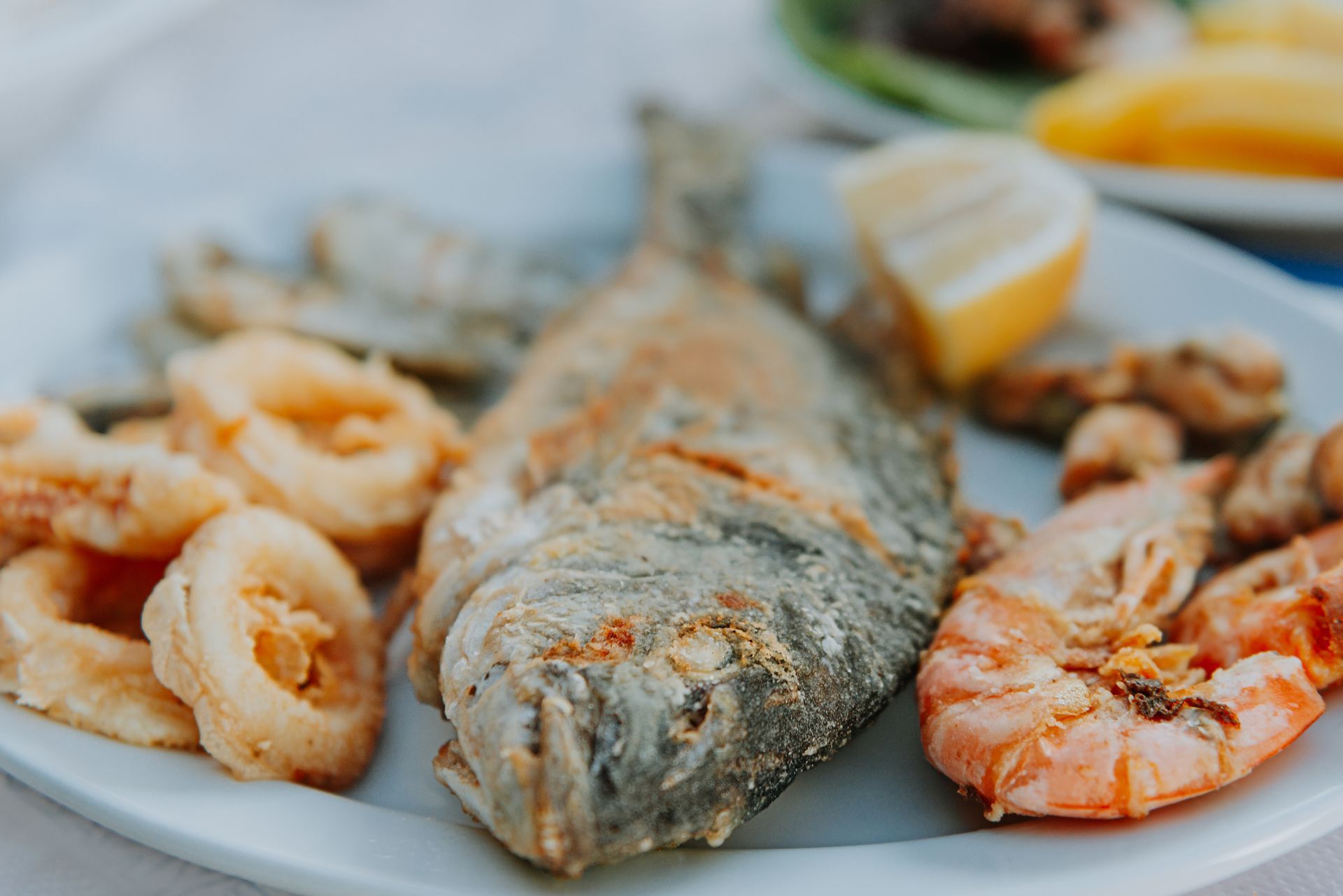 Un piatto bianco condito con pesce fritto, gamberi, calamari e fette di limone.