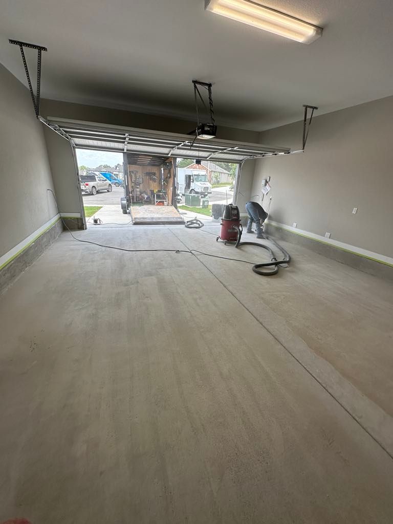 A man is working in a garage grinding concrete with a vacuum cleaner.