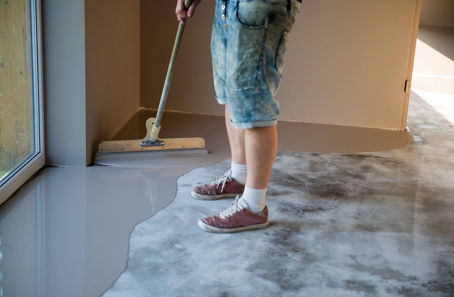 a man is spreading concrete on the floor with a mop .