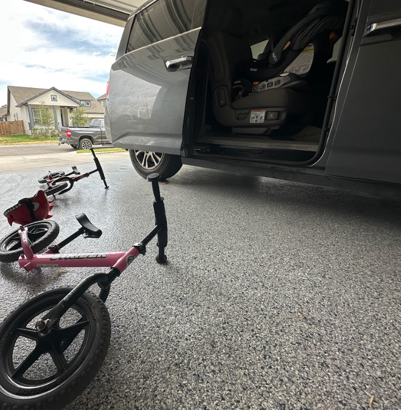 A pink balance bike is parked next to a gray van in a garage.