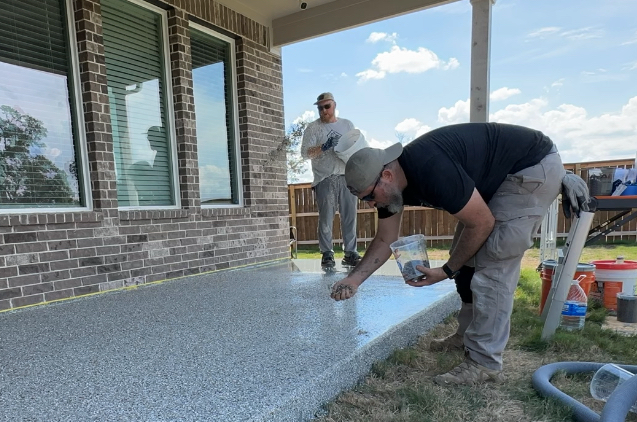 two men are painting a concrete porch in front of a brick house .