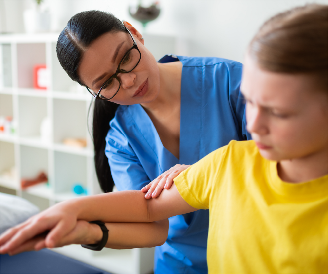 Physical therapist examining a person's arm in a clinical setting; they both have focused expressions.