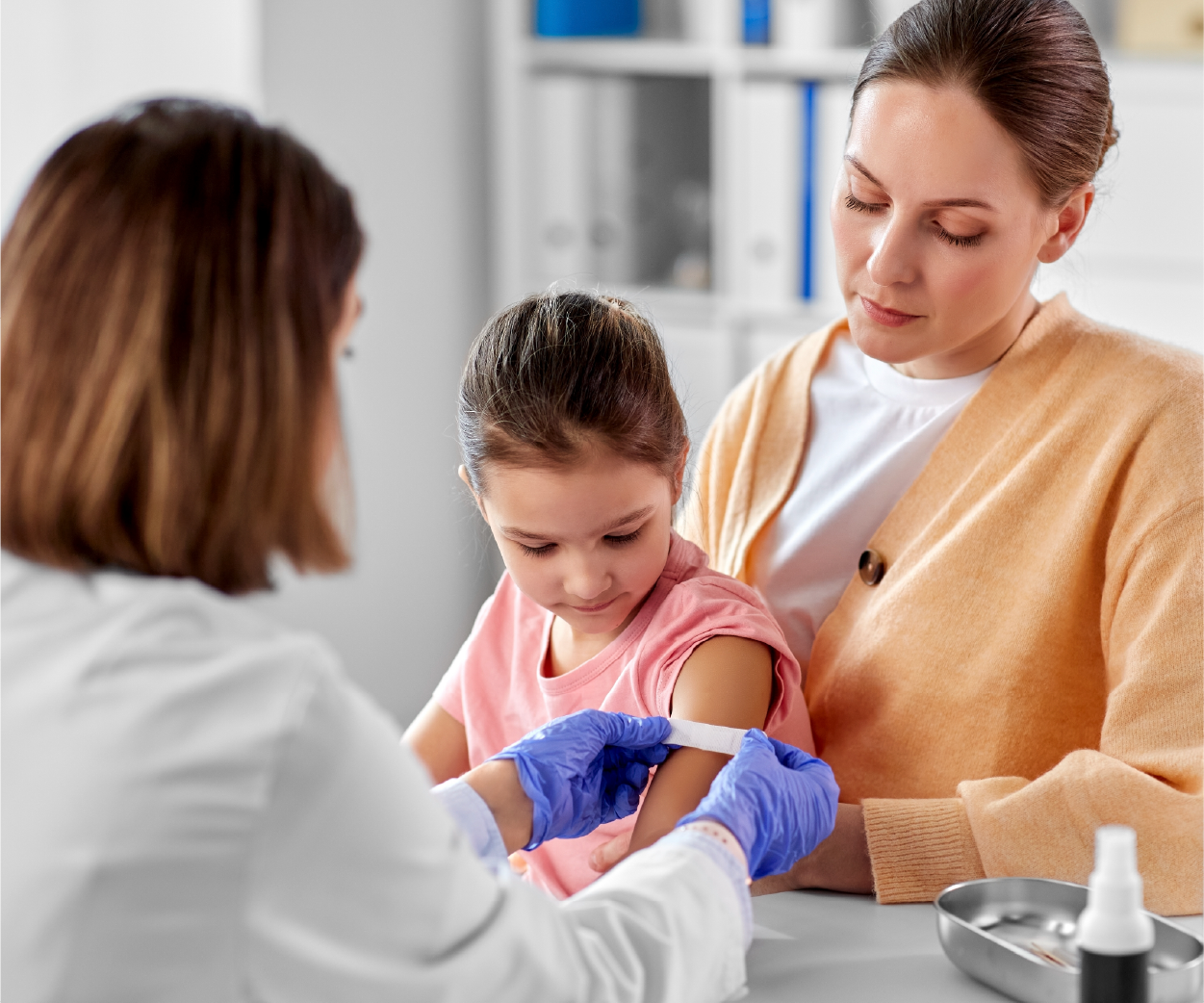 A medical professional applying a bandage to a child's arm after a vaccination. Mother looks on.