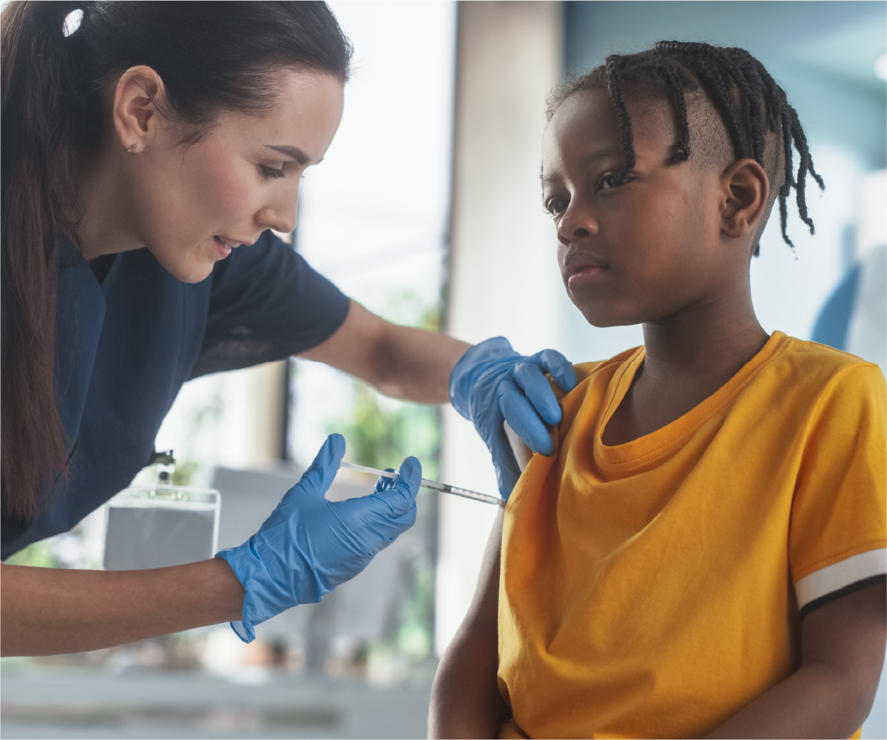 Medical professional giving a shot to a child. The child is wearing a yellow shirt and looking away.