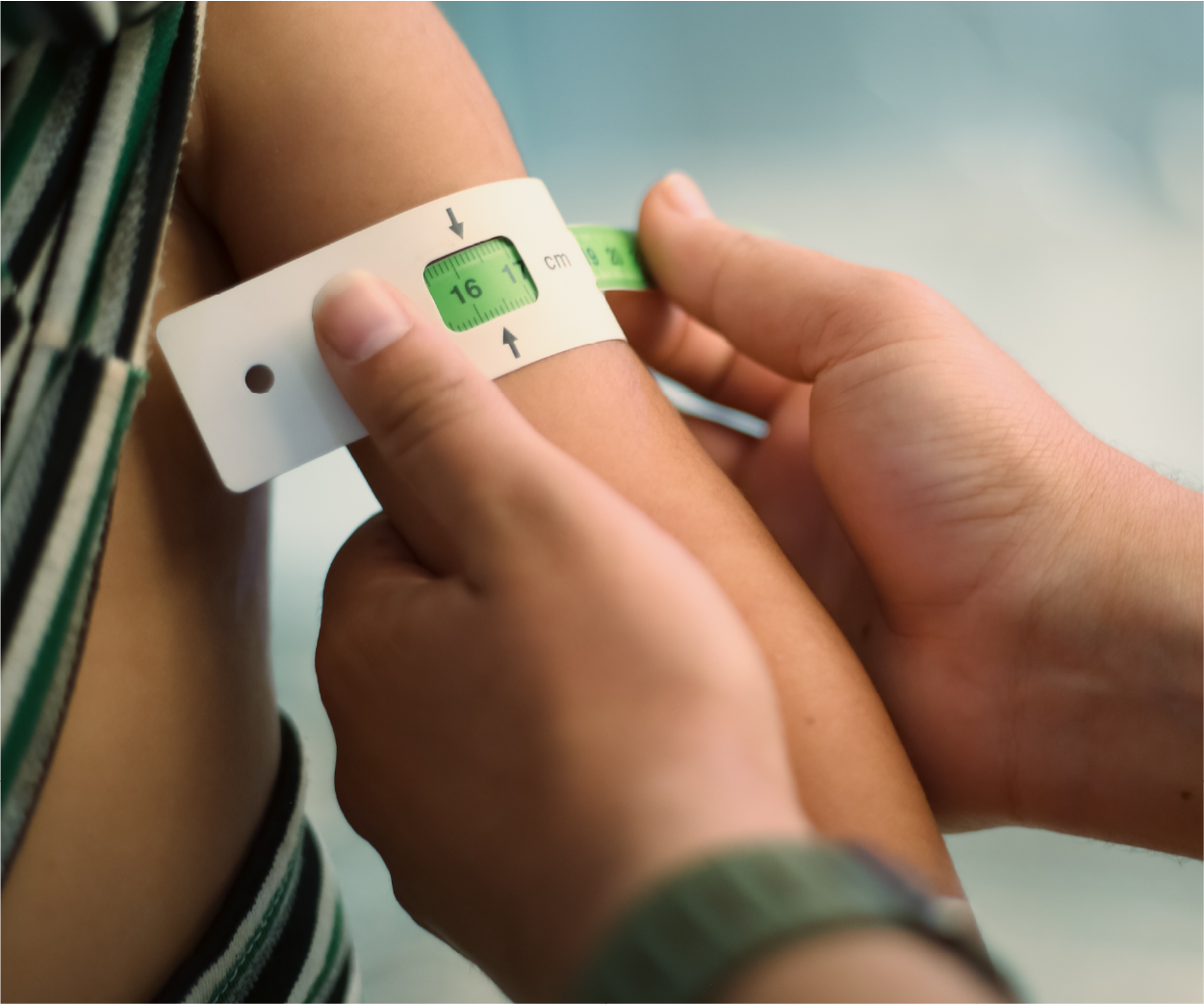 Person measuring another's upper arm with a tape and a measuring tool, for assessing nutritional status.