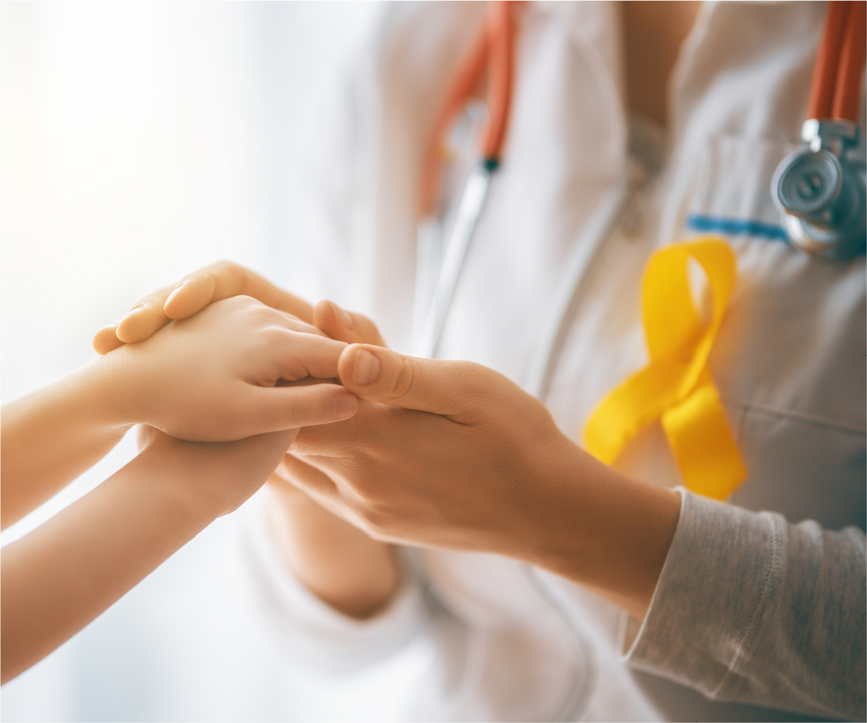 Doctor holding child's hand; yellow ribbon for childhood cancer awareness on doctor's coat.