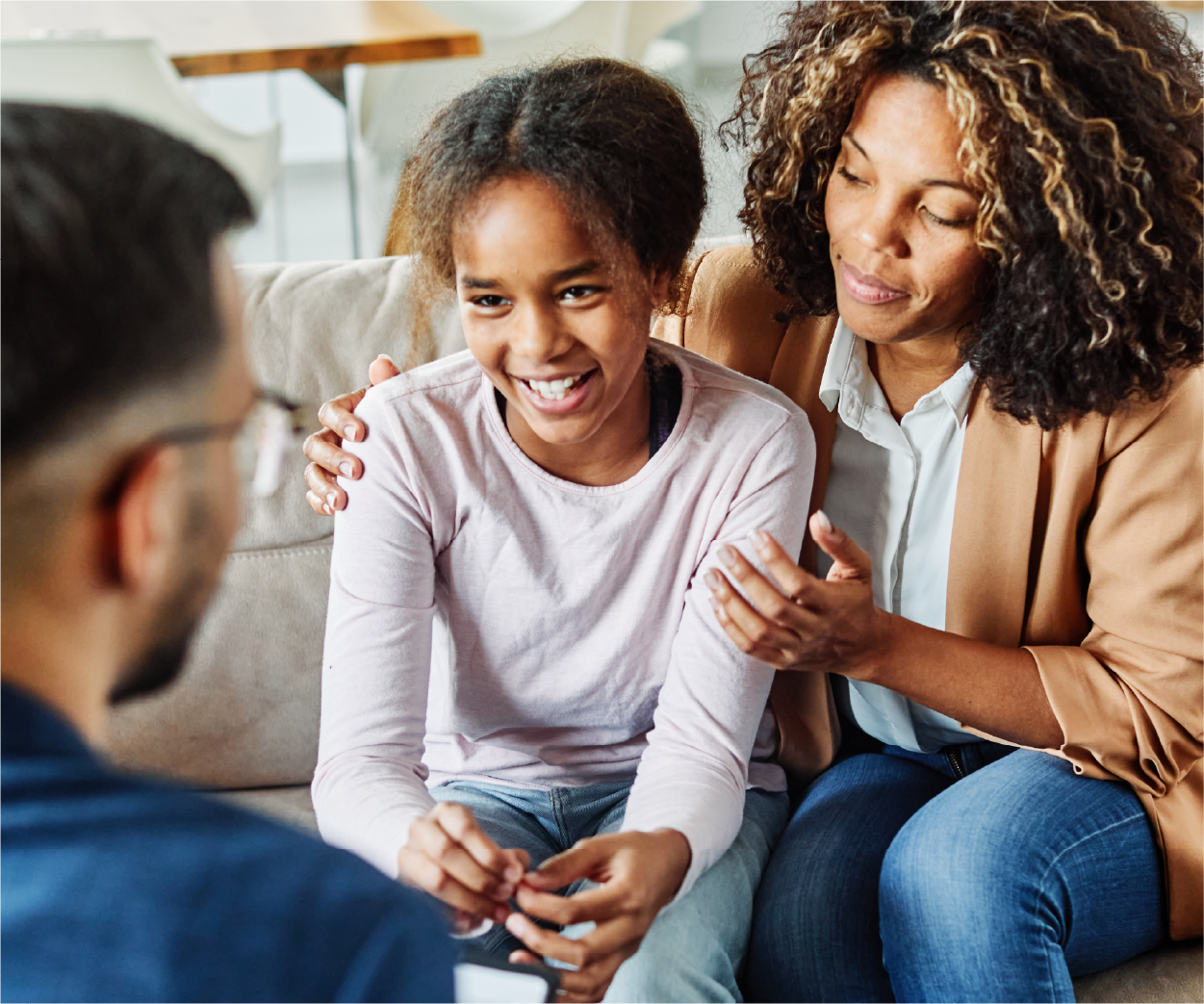 Woman and child on couch talking to a person, likely in a therapy session. The child is smiling.