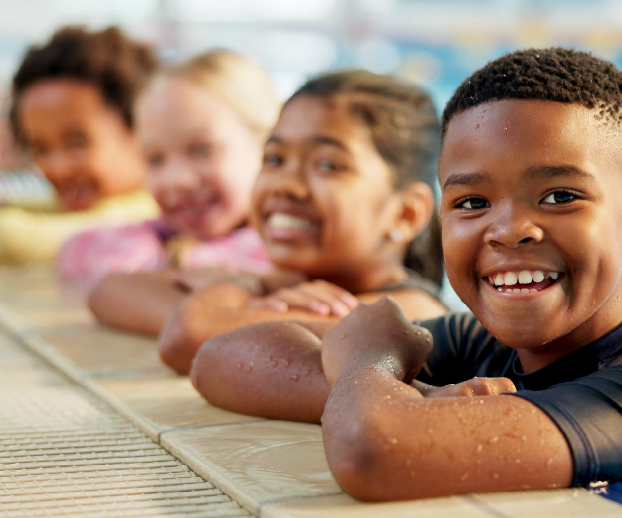 Children smiling at the edge of a pool, arms resting on the deck.