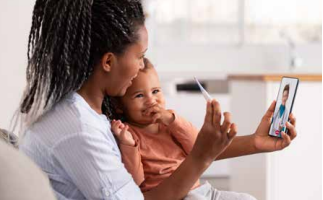 Woman holding a child while video chatting on a smartphone in a bright home kitchen