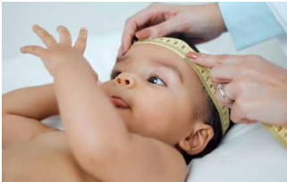 Baby being measured with a tape measure on the head by hands in a clinical setting